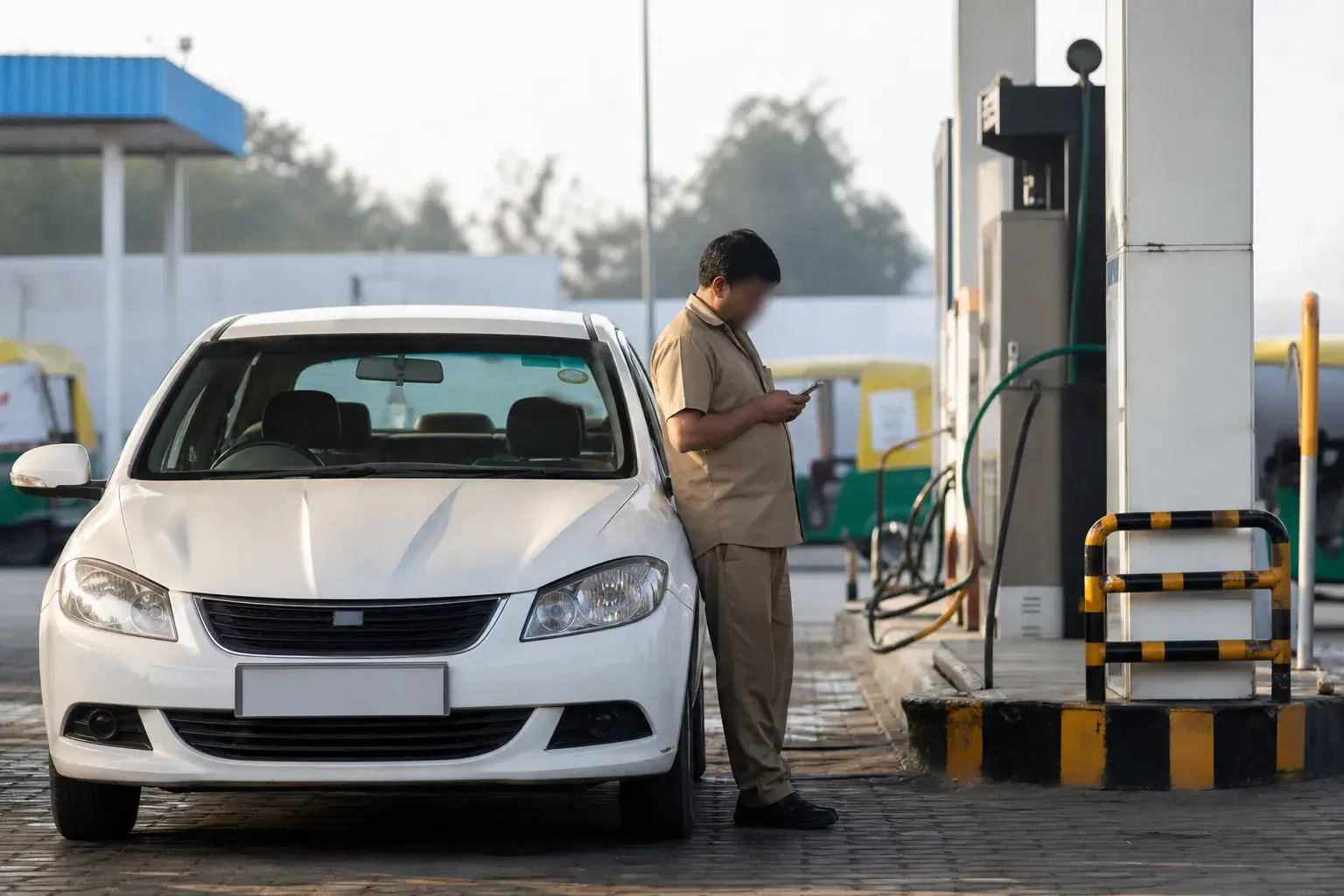 Cab driver checking fuel prices on a phone beside a car at a CNG station
