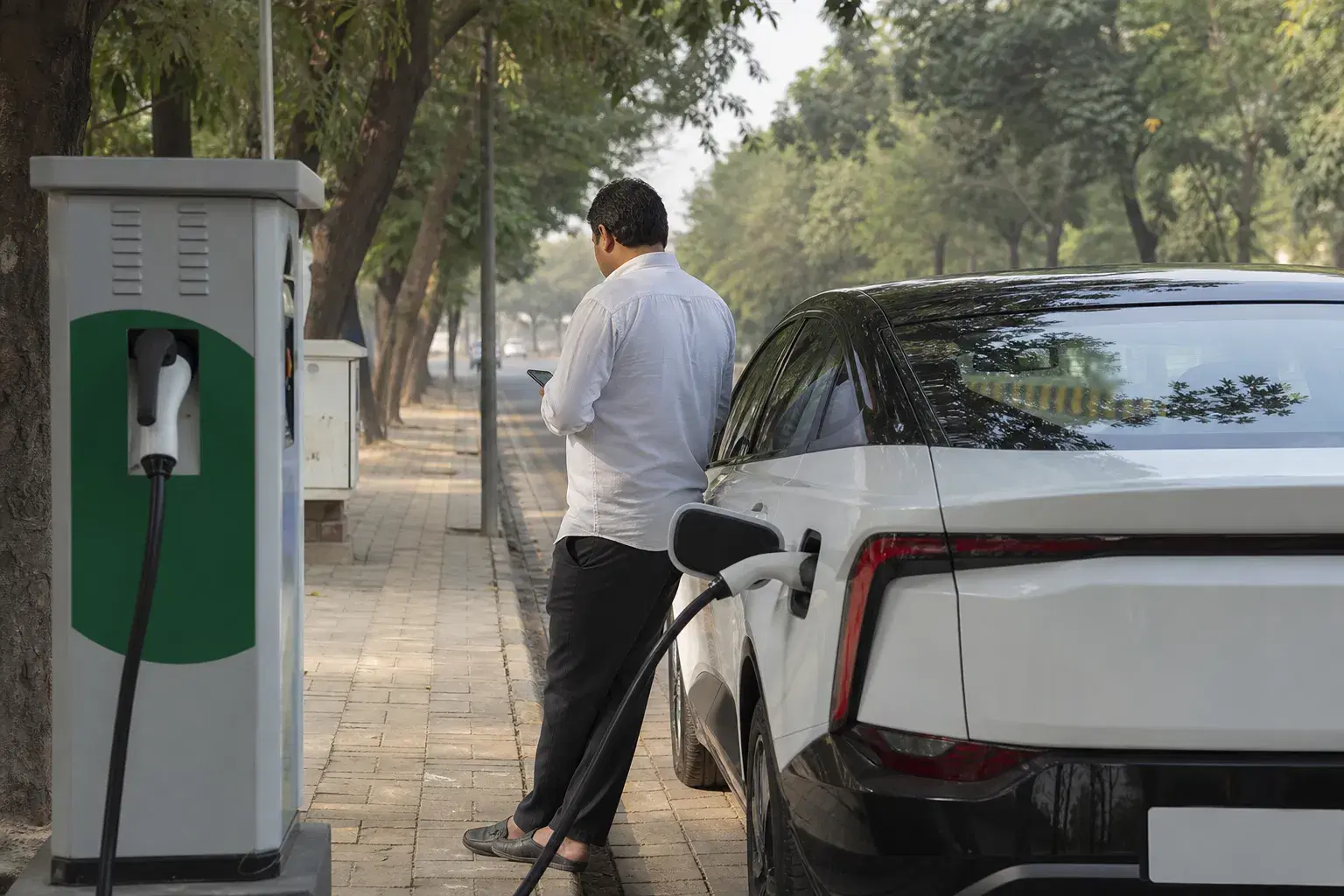 An electric cab charging while a driver checks a phone nearby